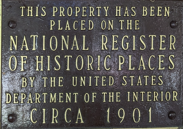 Eine Metalltafel an einem Gebäude trägt die Inschrift "Dieses Grundstück wurde in das National Register of Historic Places aufgenommen."