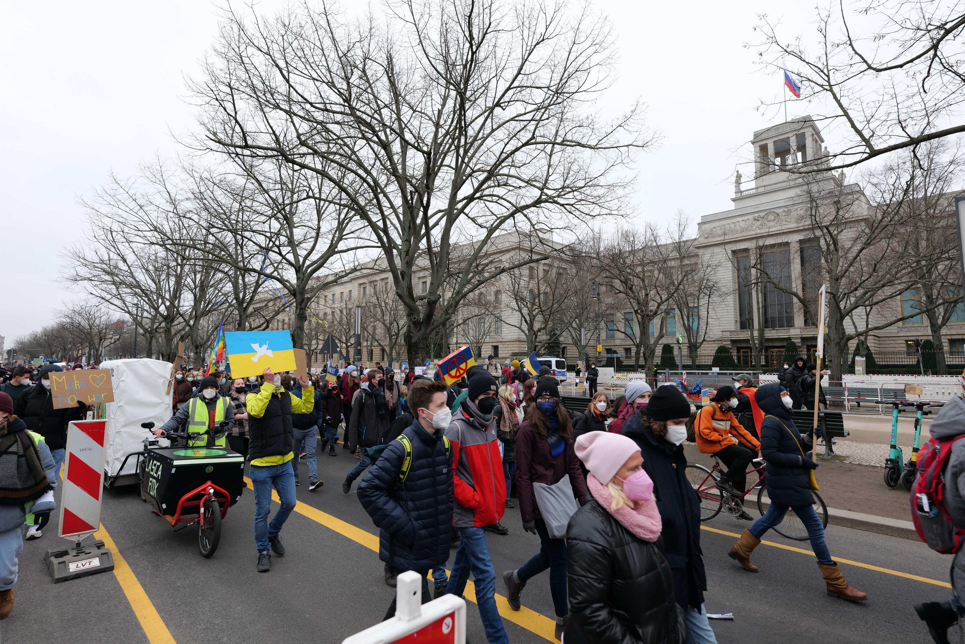 Eine große Gruppe von Menschen marschiert auf der Straße in Washington, D.C., mit Schildern und Transparenten, einige fahren Fahrräder, unter einem klaren blauen Himmel.