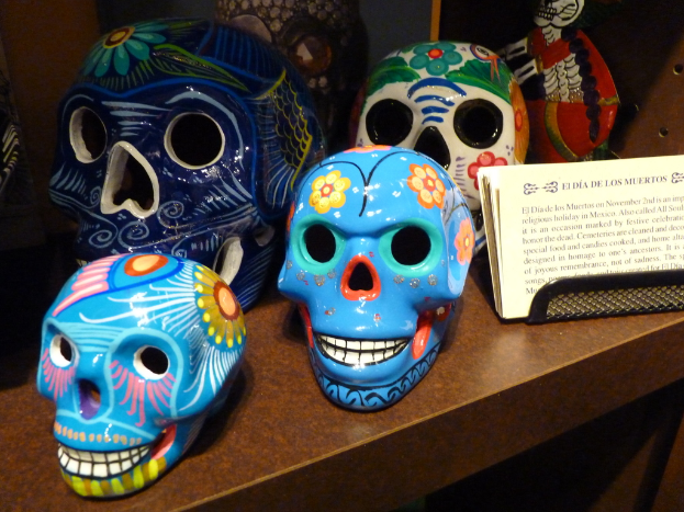 Ein Tisch mit verschiedenen farbigen Schädeln neben Papieren mit handgeschriebenen Notizen.