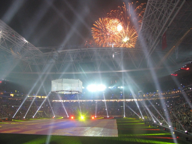 Olympiastadion in London bei Nacht, hell erleuchtet mit grünem Rasen, umgeben von einer großen Menge und Feuerwerk, das den Himmel erhellt.