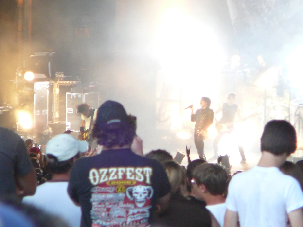 Eine Gruppe von Menschen in verschiedenen Kleidungsstücken, einige mit Mützen, in der Nähe von Musikinstrumenten wie einer Gitarre und einem Mikrofon, mit Bühnenbeleuchtung.