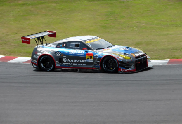 Ein Nissan GT-R Nismo GT3 Rennwagen fährt auf einer Rennstrecke mit Text auf dem Auto und Gras im Hintergrund.