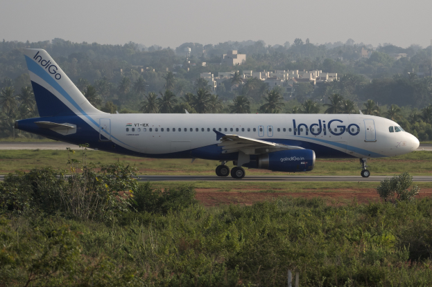 Indigo Airlines Airbus A320-200 auf der Rollbahn am Mumbai Airport mit Grünflächen, Bäumen, Gebäuden und einem klaren blauen Himmel im Hintergrund.