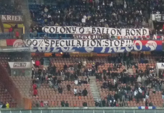 Ein Stadion voller Menschen, Fahnen und Stühle, mit einem Zaun unten und einer Treppe links.