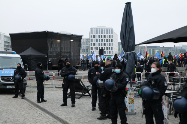 Polizeibeamte in Uniform hinter Barrieren vor einer Menge von Demonstranten, einige mit Helmen und Masken, mit Zelten, Fahnen und Gebäuden im Hintergrund während einer Demonstration in Berlin gegen Sparmaßnahmen der Regierung.