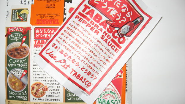 Ein Prospekt, der Pfeffersoße bewirbt, mit einem darunter liegenden Blatt, auf dem verschiedene Currys beworben werden.