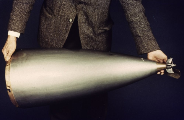 Ein Mann in einem Anzug, der ein großes metallisches Objekt hält, das wie eine Bombe aussieht.