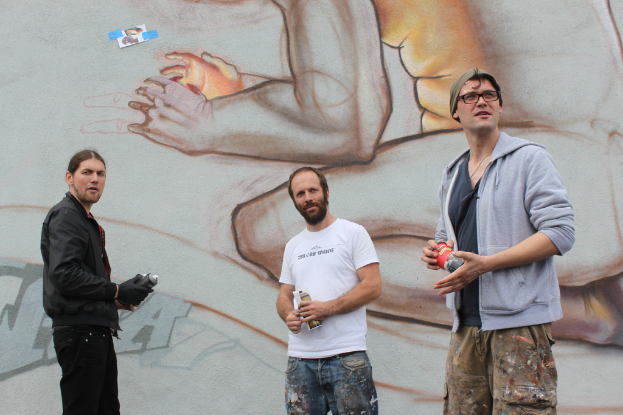 Menschen mit Farbsprühflaschen in den Händen vor einer Graffiti-Wand