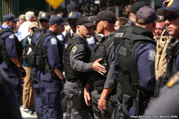 Eine Gruppe von Polizisten in Uniform, die auf einer Straße stehen, einige mit Waffen, mit Gebäuden und Schildern im Hintergrund.