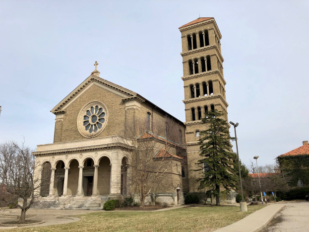 Die Basilika des Heiligen Herzens Jesu in St. Louis, Missouri, eine große Kirche mit einem zentralen Glockenturm, umgeben von Gebäuden, Straßenlaternen, Fahrzeugen, Bäumen und einem bewölkten Himmel.