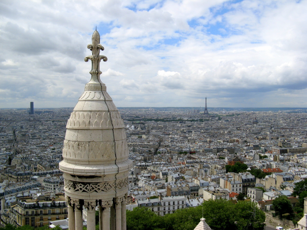 Luftaufnahme einer Stadt mit Gebäuden, Türmen, Bäumen und einem bewölkten Himmel.