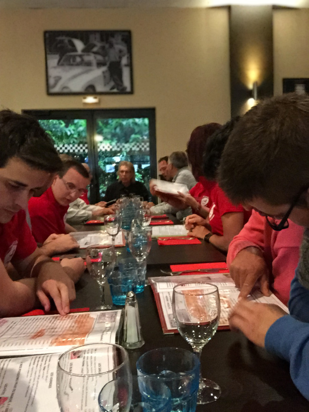 Eine Gruppe von Menschen, die auf StÃ¼hlen um einen Tisch sitzen und WeinglÃ¤ser darauf haben.