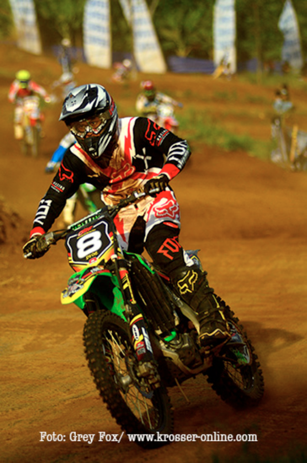 Mehrere Motorradfahrer bei einem Rennen, alle mit Helmen, mit Text am unteren Bildrand.