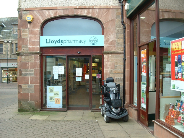 Eine Apothekenfiliale mit einem Fahrzeug davor und einem Geb├Ąude in der linken Ecke.