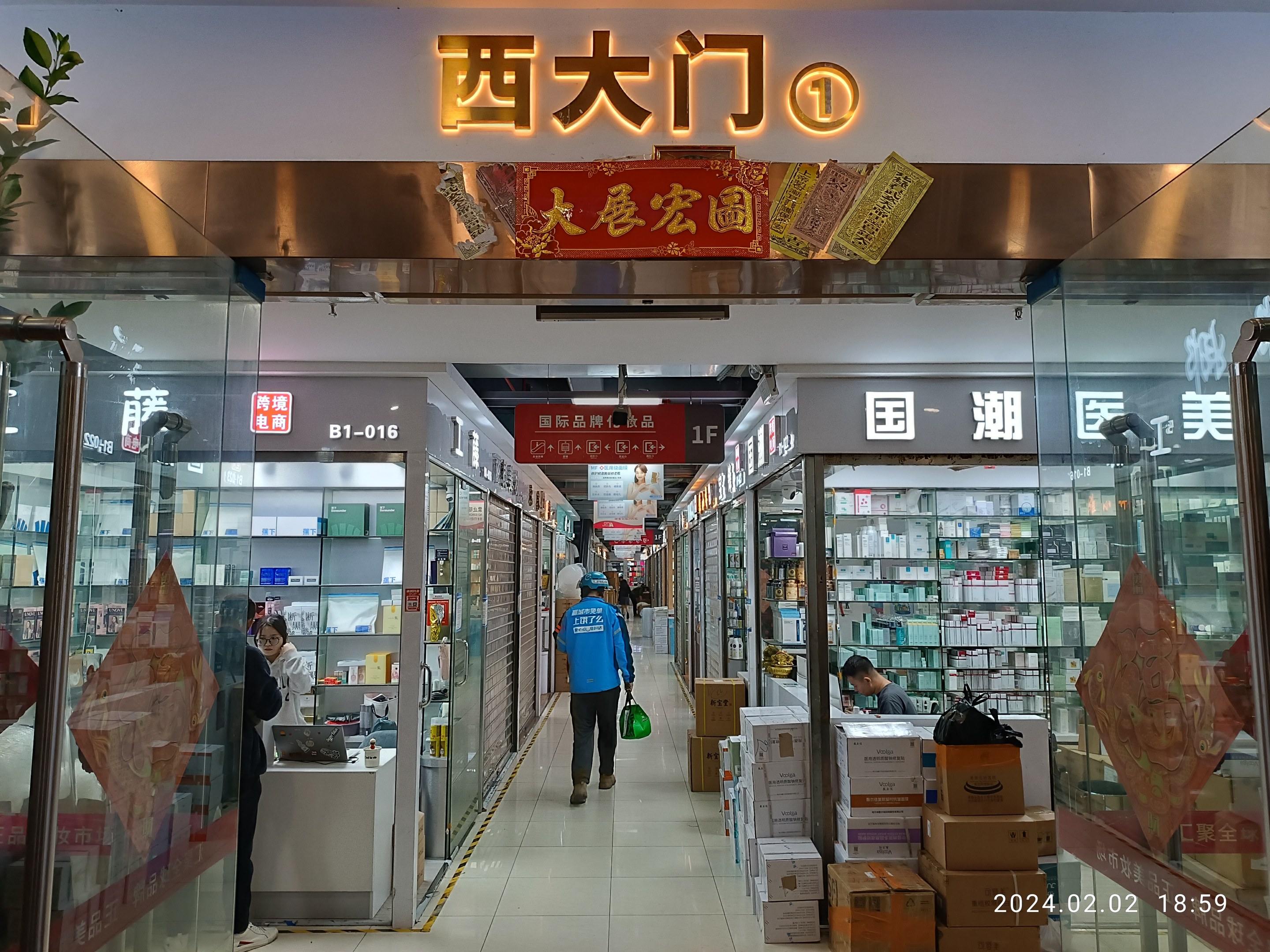 Innenseite einer chinesischen Apotheke mit Glaswänden, einer Pflanze links, Regalen voller Gegenstände, verstreuten Kartons und einem Namensschild oben.