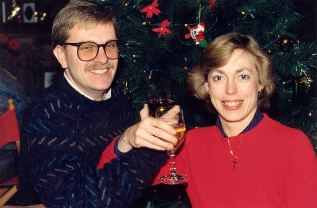 Ein Paar lächelt beim Glas Wein halten, mit einem Weihnachtsbaum im Hintergrund.