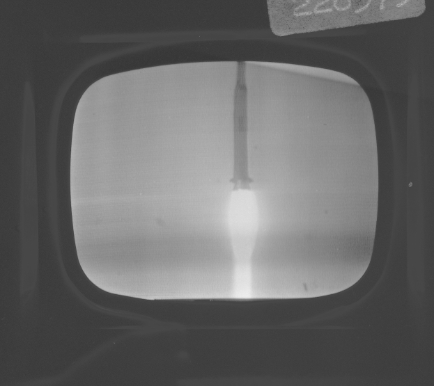 Schwarzes und weißes Foto eines Fernseherbildschirms, der eine Raketenstarts zeigt, der durch sein Fenster sichtbar ist, mit Text oben.