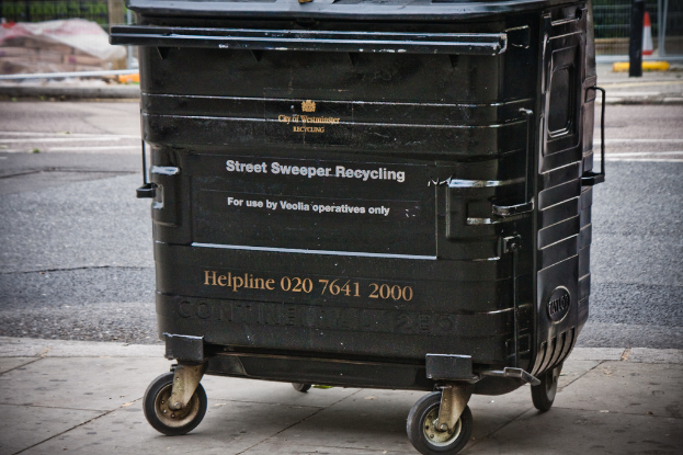 Ein schwarzer Mülltonne steht in der Mitte des Bildes mit einer Straße unten.