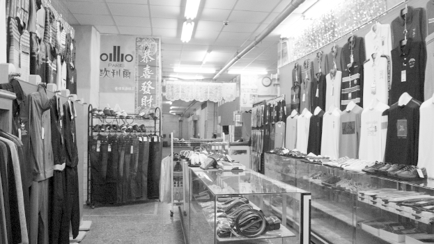 Eine Anzeige von Kleidung, Gürteln und Schuhen mit einer Uhr an der Wand, hängendem Stoff, Lampen darüber und einem Banner mit Text auf der linken Seite.