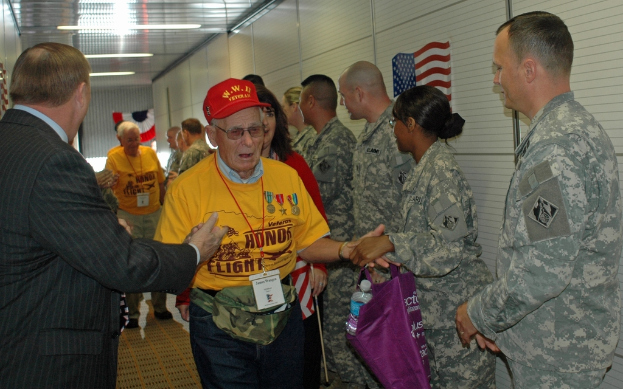 Eine Gruppe von Menschen und Soldaten steht drinnen mit einer Flagge auf der rechten Wand und Lichtern an der Decke.