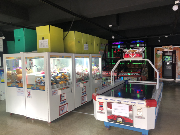 Ein Raum voller verschiedener Arcade-Spiele, einschließlich eines Spielautomaten auf der rechten Seite, einem sichtbaren Boden und Deckenlampen.