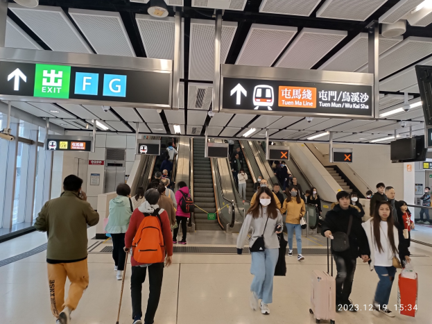 Menschen mit Gep├Ąck durch einen geschlossenen Flughafen gehen, mit Rolltreppen, Fluginformationsbildschirmen, Deckenleuchten und Glasw├Ąnden im Hintergrund.