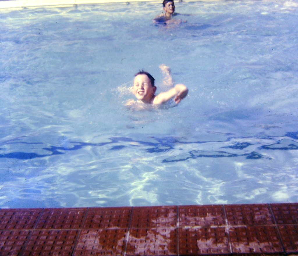 Schwarzes und weißes Foto von drei Kindern, die im Wasser schwimmen, mit einer Wand im Hintergrund.