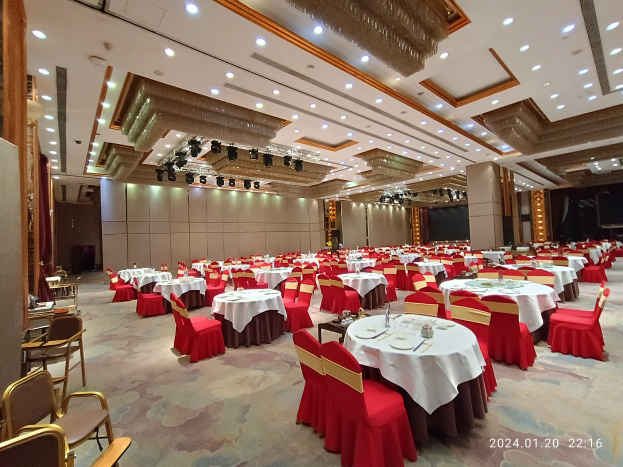 Großer Ballsaal mit weiß gedeckten Tischen, Gläsern, Tellern, Besteck und Dekoration an den Wänden sowie beleuchteter Decke, mit Wasserzeichen unten rechts.