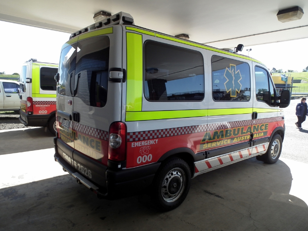 Zwei Rettungswagen nebeneinander unter einem Dach geparkt, mit einer Person auf der rechten Seite und einem Mann neben dem linken Rettungswagen.