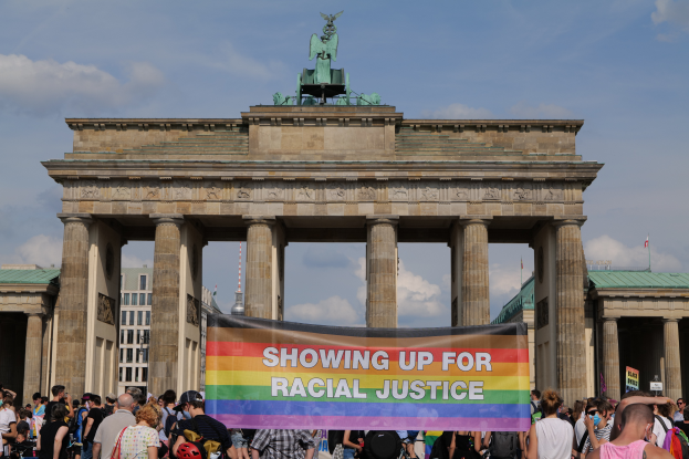 Eine Gruppe von Menschen steht vor dem Reichstagsgebäude in Berlin, Deutschland, mit einer Tafel, auf der 'Rassengerechtigkeit' steht.