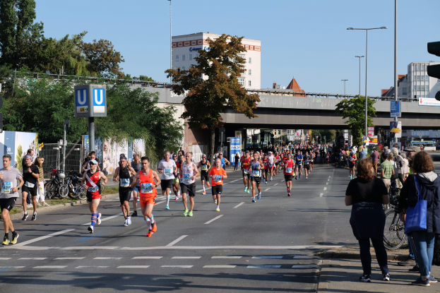 Eine Gruppe von Menschen, die bei einem Marathon auf einer von Bäumen gesäumten Straße unter einem klaren blauen Himmel laufen.