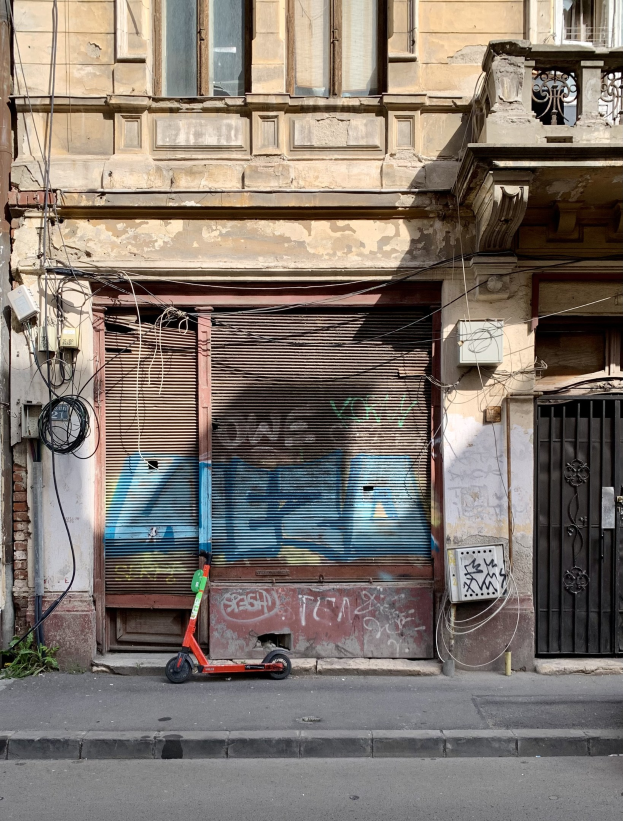 Ein roter Roller, der auf der Straße neben einem Gebäude mit Fenstern, Rollläden und einem Tor geparkt ist.
