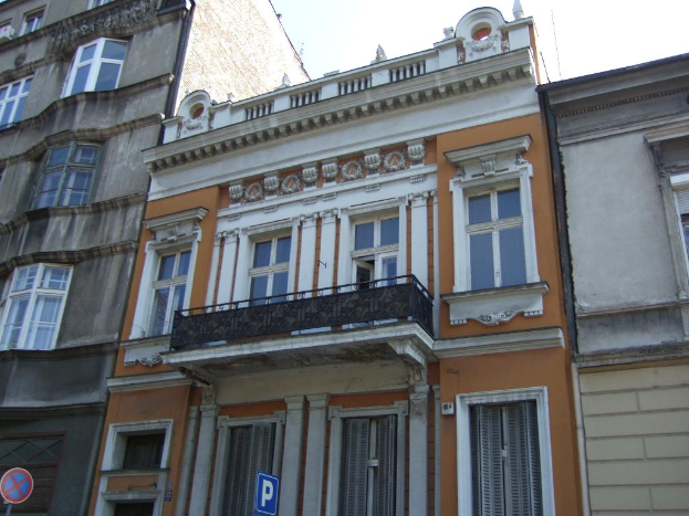 Mehrere Gebäude mit Türen und Fenstern, klarer Himmel und Warnschilder an Pfählen.