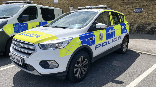 Zwei Polizeiwagen nebeneinander auf einem Parkplatz geparkt, mit einer Wand und einer Tafel im Hintergrund.