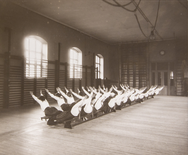 Menschen, die Pilates-Übungen in einem Fitnessstudio mit einer Uhr an der Wand ausführen.