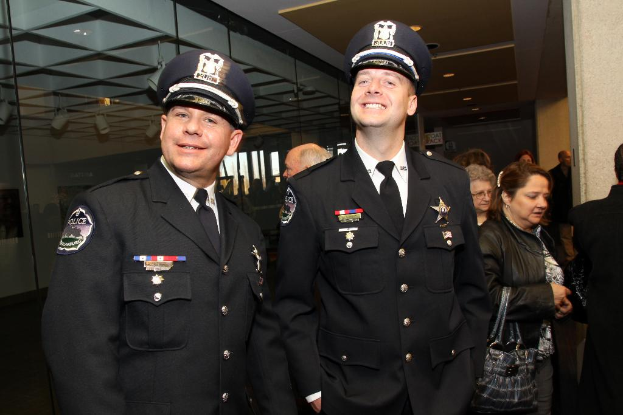 Zwei Beamte mit strahlendem Lächeln im Vordergrund, Menschen in der Mitte, Glasfenster links, Lampen und Decke oben und Säulen und Menschen rechts.