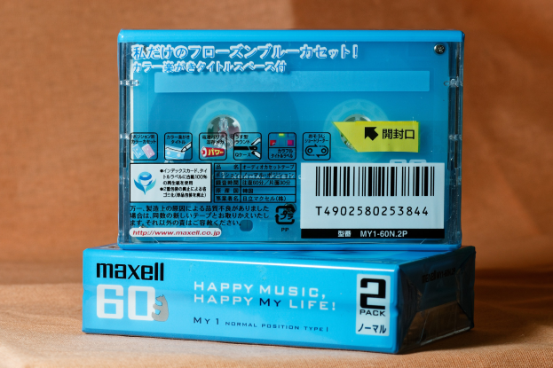 Blaue Maxell-Kassette mit der Aufschrift "Happy Music Happy My Life" auf einem braunen Tisch mit einem weich unscharfen Hintergrund.
