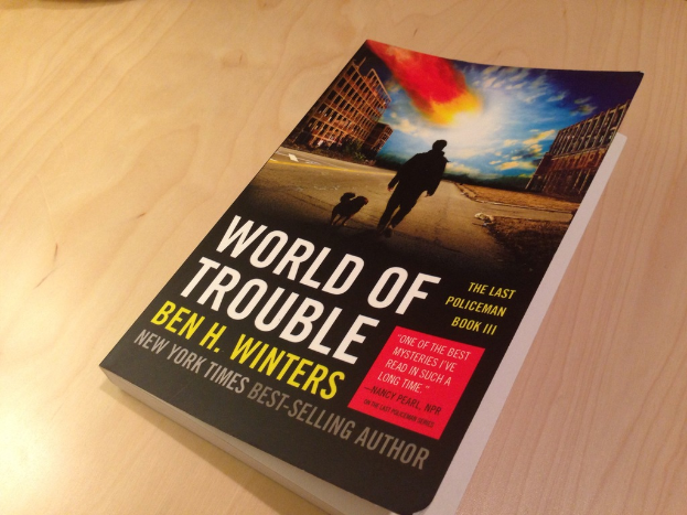 Ein Buch mit dem Titel "World Of Trouble", das einen Mann und einen Hund auf dem Cover zeigt, das auf einem Tisch liegt.