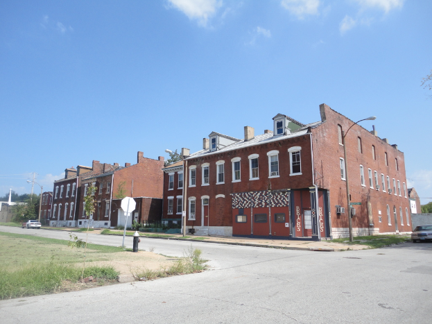 Ein Gebäude mit Straßenlaternen, Bäumen und Fahrzeugen auf beiden Seiten, einem Gehweg und Gras unten und einem Himmel oben.