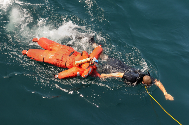 Retter in einer orangen Schwimmweste, der an einem Seil über dem Wasser hängt.