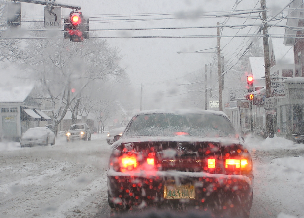 Eine schneebedeckte Straße mit wenigen Fahrzeugen, gesäumt von schneebedeckten Bäumen und Häusern auf beiden Seiten.
