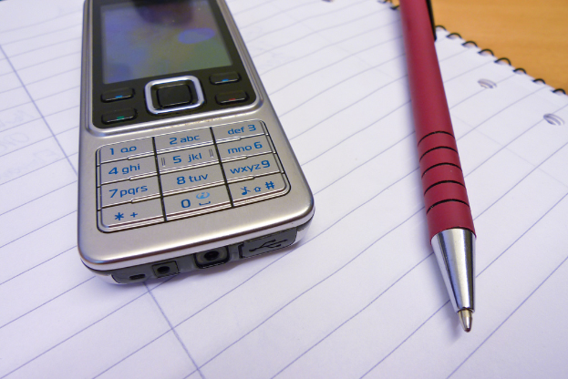 Ein Mobiltelefon und ein Stift liegen auf einem aufgeschlagenen Buch.