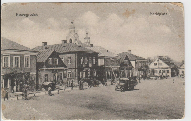 Schwarze und Weiße Fotografie einer Straße in Nowogrodziec, Deutschland, mit Gebäuden, Menschen, Wagen, Pföhlen, Bäumen und Himmel sowie dem Text "Marktplatz in Nowogrodeek, Deutschland" oben und unten.