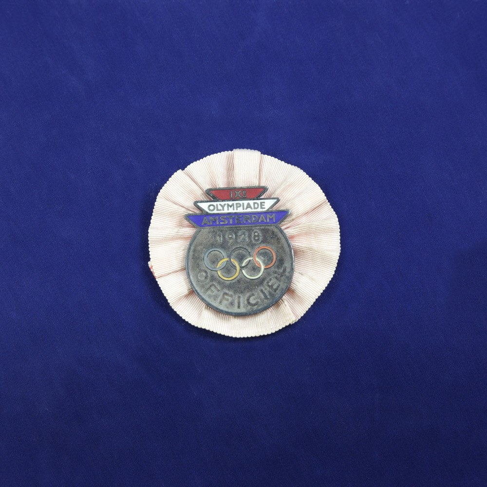 Blauer Stoff mit einem zentralen Olympic-Logo-Abzeichen, das wahrscheinlich eine Medaille anzeigt.