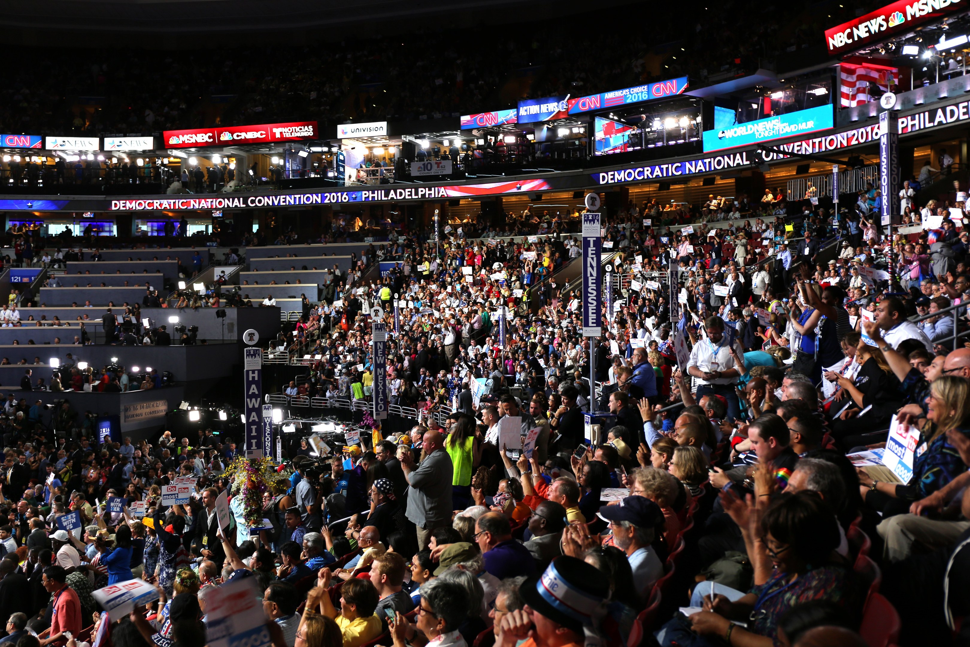 Große Menschenmenge vor einer beleuchteten Bühne auf der Democratic National Convention 2016 in Philadelphia, viele halten Schilder, mit Stufen und Texttafeln um die Bühne herum.