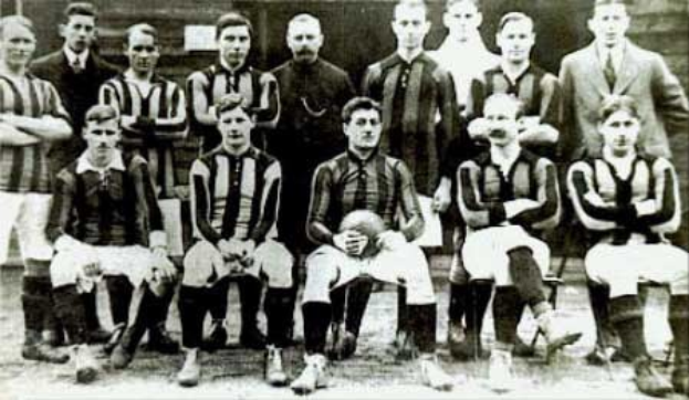 Schwarzes und wei├čes Foto einer Fü├čballmannschaft, einige stehen, einige sitzen, vor einer Wand mit dem Text "Ballymena Football Club" unten.