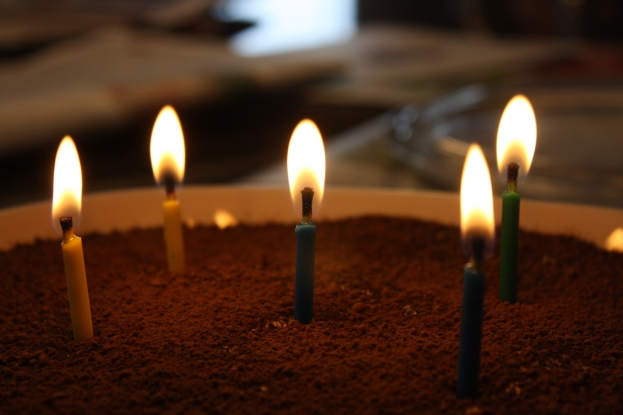 Eine Ausstellung mit einem Tisch, auf dem verschiedene Landesflaggen, eine Box, Papiere und ein Banner liegen, eine Kugel zur Linken, eine Anschlagtafel zur Rechten mit einigen Menschen in der Nähe und mehreren Tischen und Stühlen links.