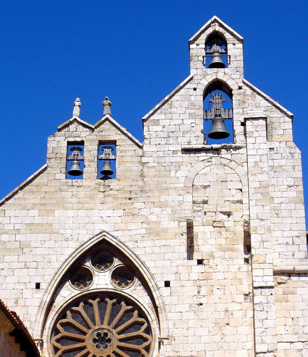 Eine alte steinerne Kirche mit zwei Glocken oben drauf, umgeben von einem klaren blauen Himmel, geschmückt mit kunstvollen Verzierungen und Designs, mit den Glocken, die laut läuten.