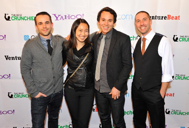 Eine Gruppe lächelnder Menschen, die für die Kamera posen, mit einem Sponsorenbanner im Hintergrund.