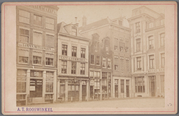 Ein Schwarz-Weiß-Foto einer Stadtstraße mit Gebäuden, die Fenster, Türen und Schilder zeigen, mit Text am unteren Rand.